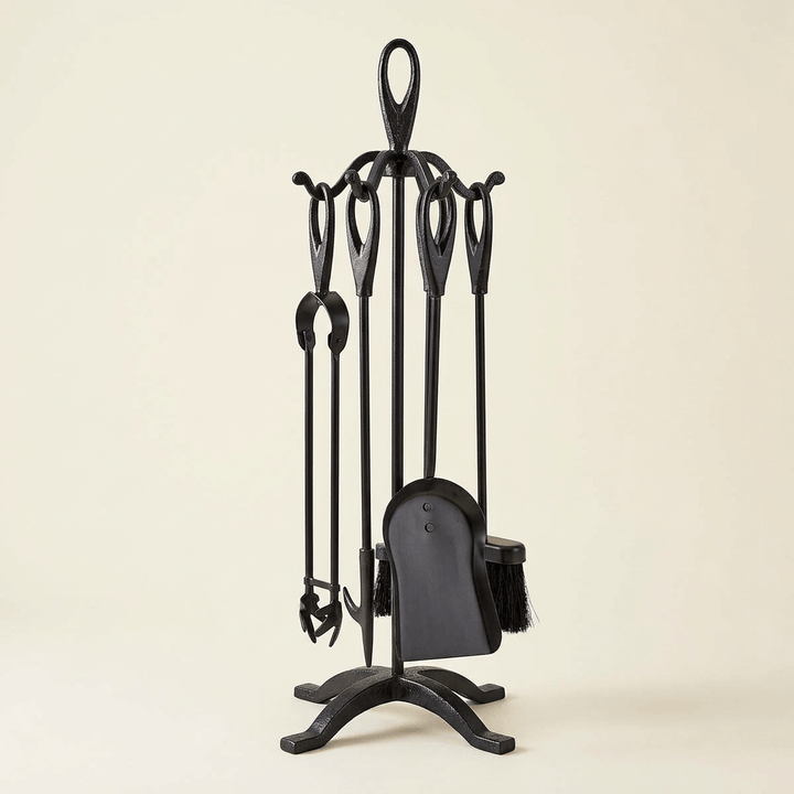 Black wrought iron fireplace tool set with four hanging tools and a freestanding stand on an ivory background