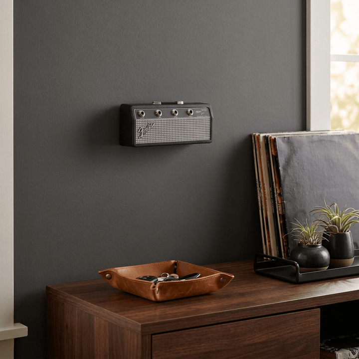 Fender amp key holder on a charcoal entryway wall above dark wood furniture with vinyl records and a leather catchall.