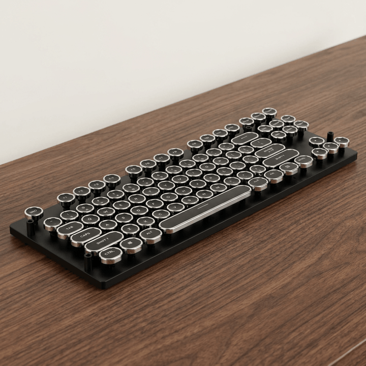 Black wired typewriter-style mechanical keyboard with silver-rimmed round keys on a walnut desk; cable out of view.