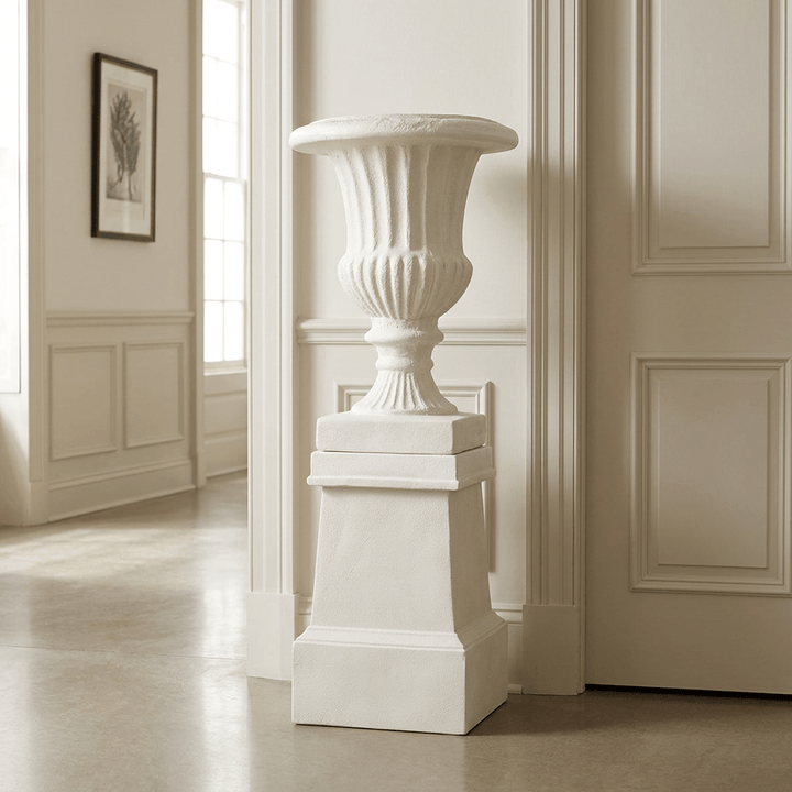 Ashbourne Fluted Urn Planter with Pedestal in Soft White, displayed full length in a light-filled paneled gallery hall.