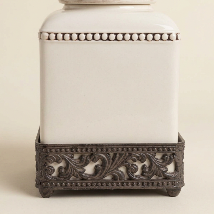Close view of Bellavita canister showing cream ceramic, beaded trim and dark acanthus-scroll base.