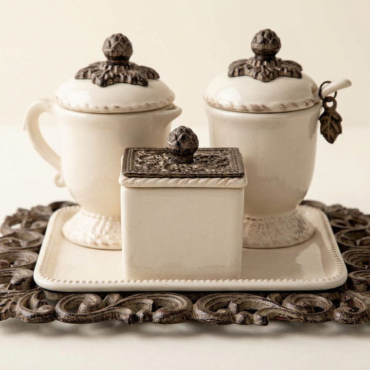 Closer view of Bellavita sweetener box, cream ceramic vessels and ornate acanthus metal tray.