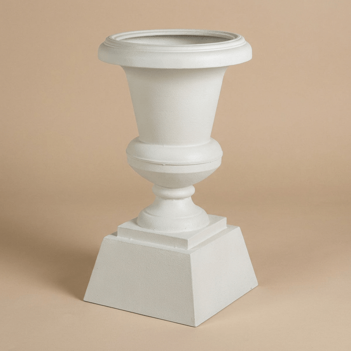 Hawthorne Aged Iron Urn Planter in Soft White against a beige studio background, showing its broad rim and stepped square base.