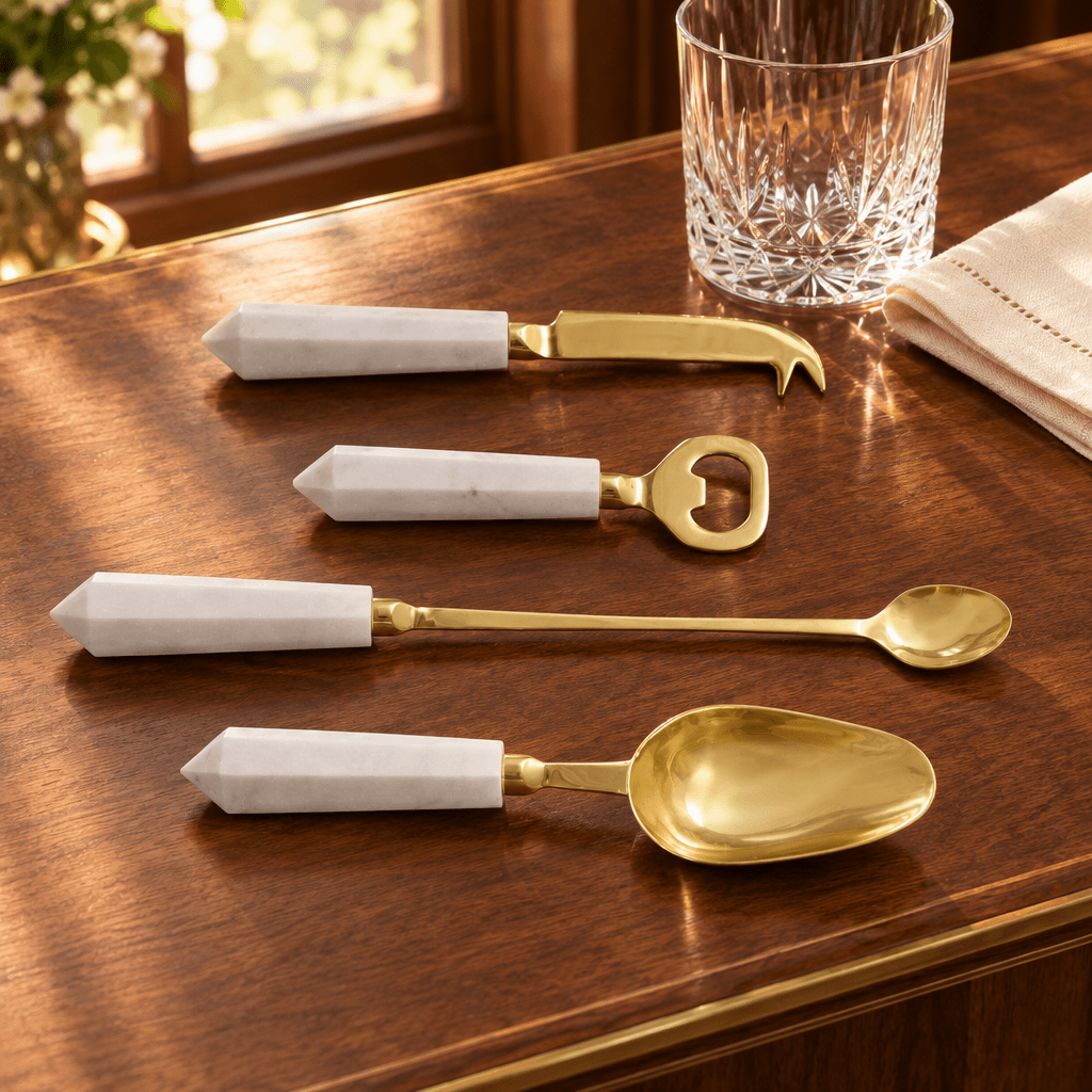 White marble and gold cocktail tool set styled on a walnut bar beside crystal glassware.