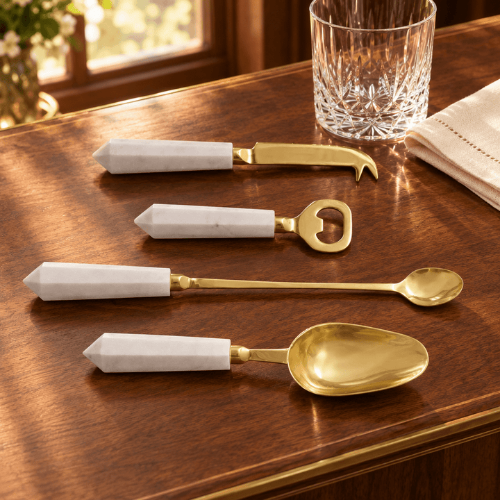 White marble and gold cocktail tool set styled on a walnut bar beside crystal glassware.