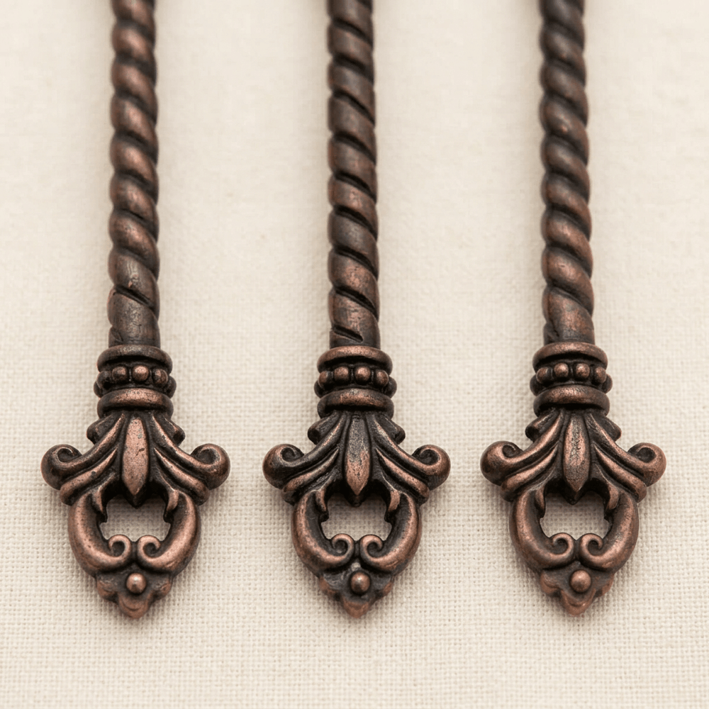 Close-up of twisted dark brass handles, beaded collars and openwork fleur-de-lis ends on the Bellavita serving set.