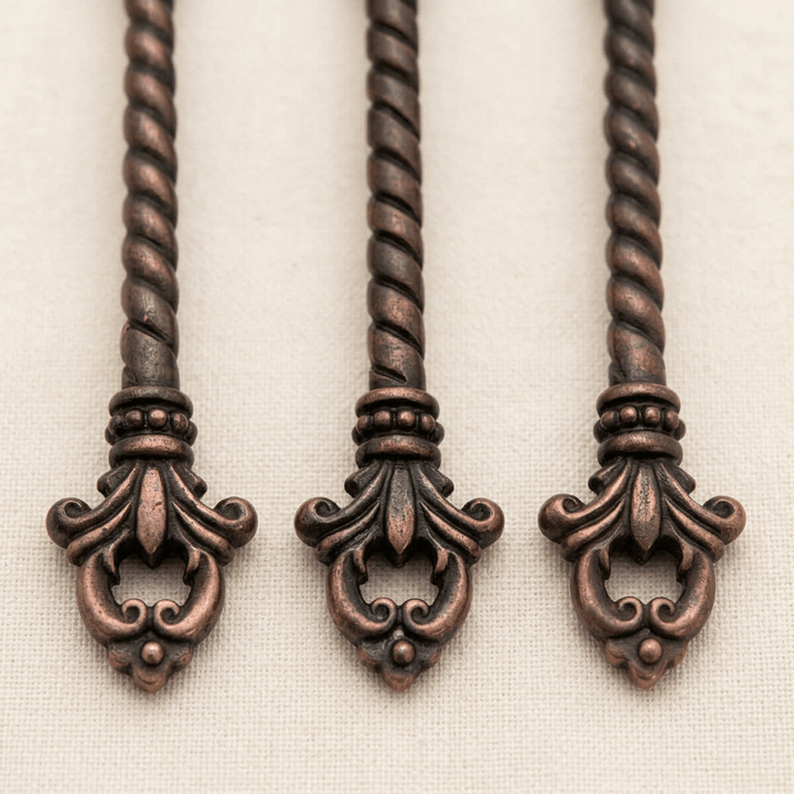 Close-up of twisted dark brass handles, beaded collars and openwork fleur-de-lis ends on the Bellavita serving set.