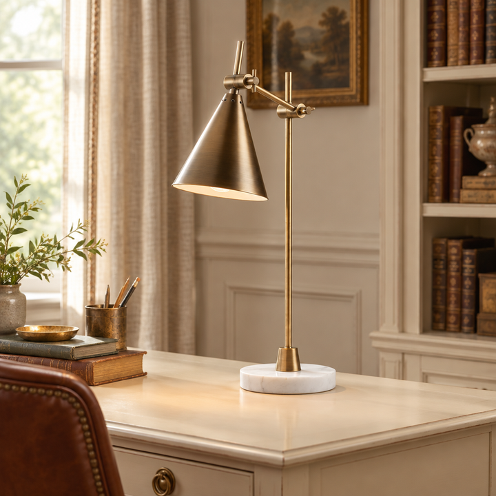 Adjustable brass-finish desk lamp with conical shade on a cream desk in a traditional study.