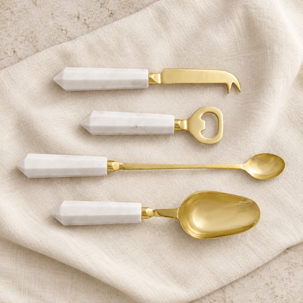 Four white marble-handled gold cocktail tools arranged on ivory linen.