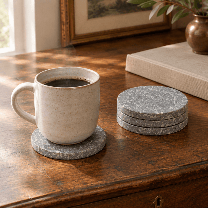 Round gray marble coasters styled with a ceramic coffee cup on a wooden writing desk.