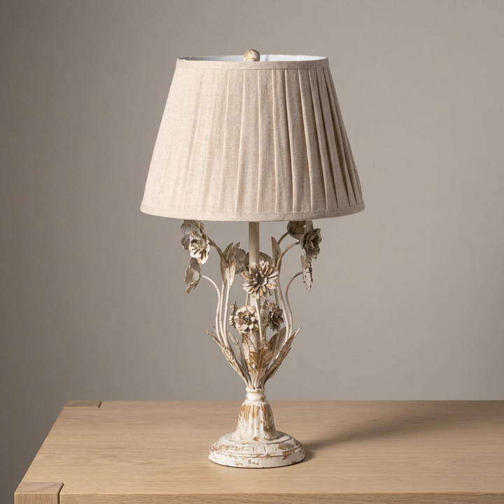 Antique White Floral Table Lamp on a pale oak surface, showing its distressed finish and full floral silhouette.