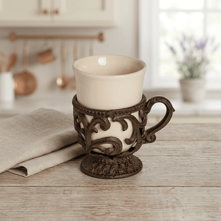 Bellavita cream ceramic coffee cup with dark brown acanthus metal holder on a wood surface beside folded linen