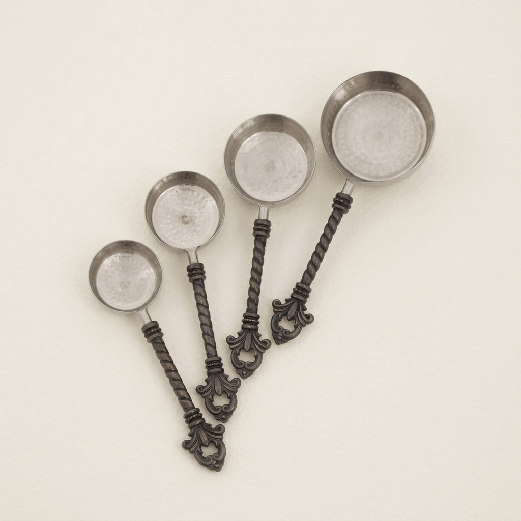 Four Bellavita measuring cups with stainless steel bowls and ornate dark handles on ivory