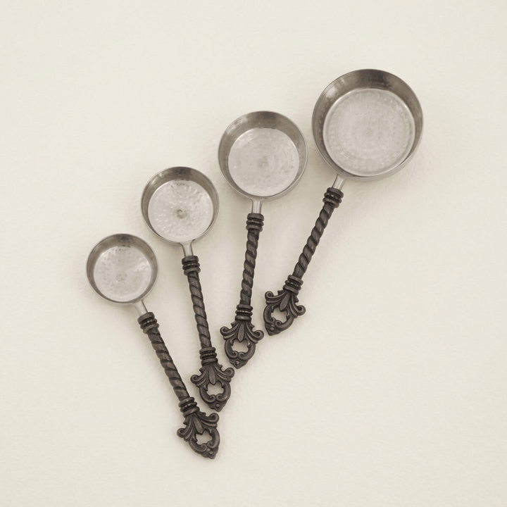 Four Bellavita measuring cups with stainless steel bowls and ornate dark handles on ivory