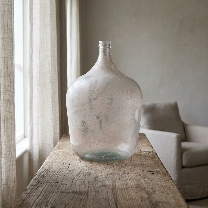 Misted Glass Demijohn Vase on a rustic wooden console beside sheer linen curtains in a softly lit neutral living room.