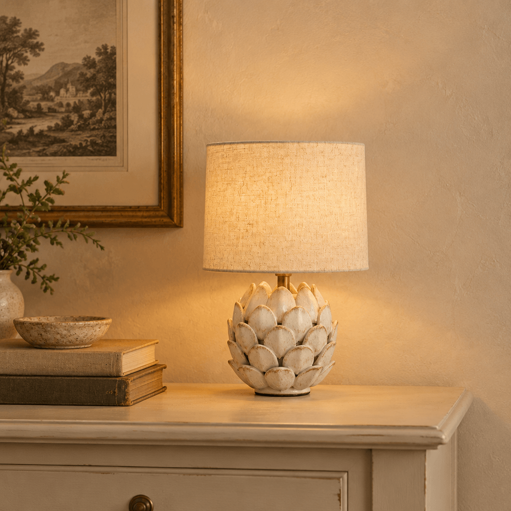 Antique white artichoke mini lamp glowing on a cream console beside books and a vintage framed print