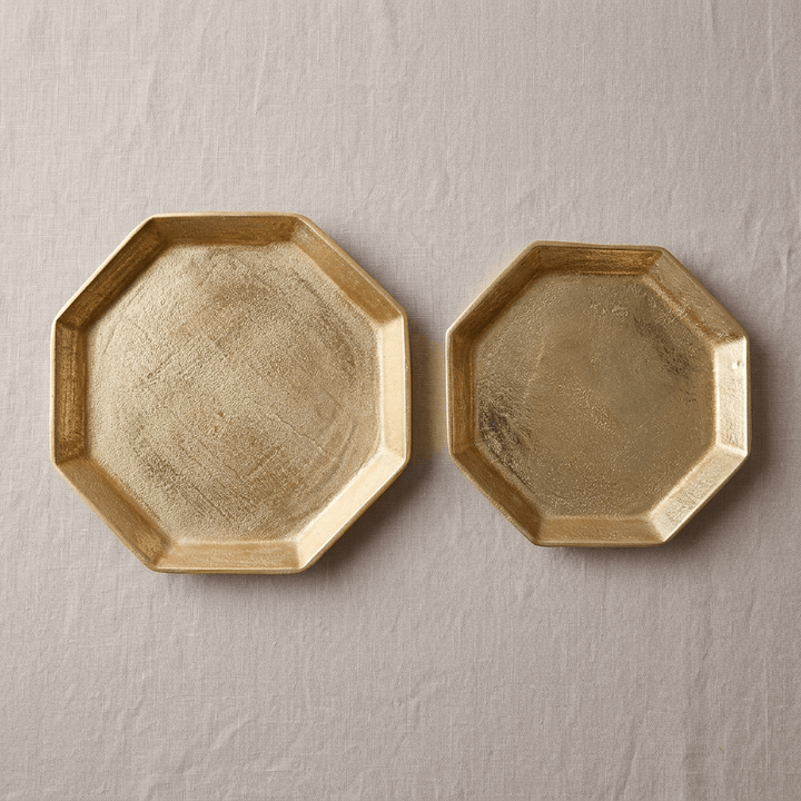 Overhead view of two gold octagonal serving trays showing their textured cast aluminum surfaces and angular rims.
