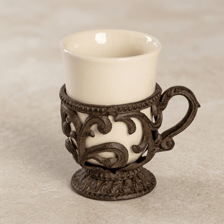 Close view of a Bellavita coffee cup showing cream ceramic and dark brown scrolling metalwork with a pedestal base