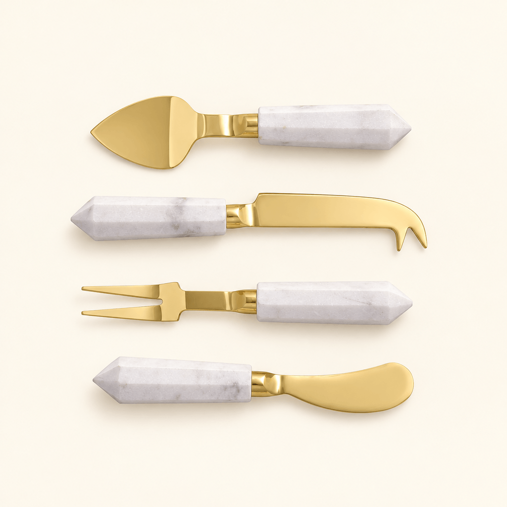 Four gold-finished cheese utensils with faceted white marble handles on an ivory background