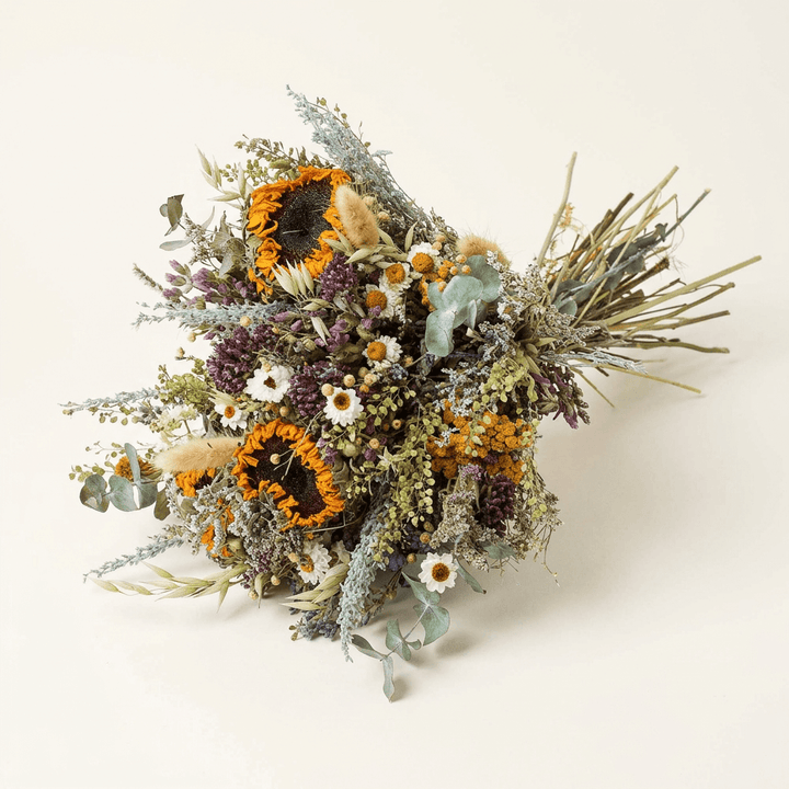 Dried sunflower and eucalyptus bouquet with white daisies and yarrow on a warm white studio background.