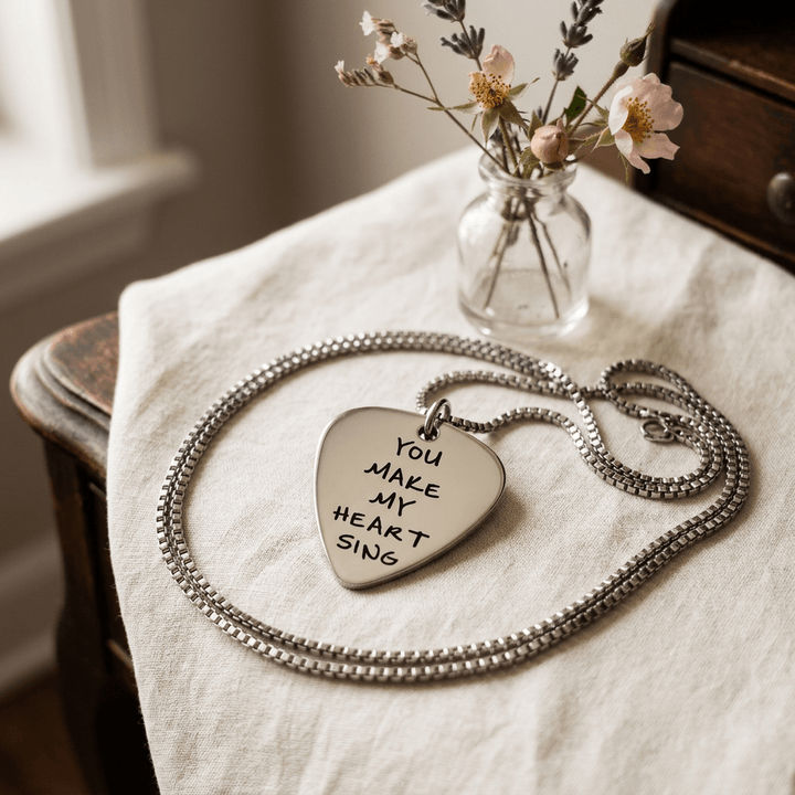 Stainless steel guitar-pick pendant and box chain arranged on cream linen on a vintage vanity.