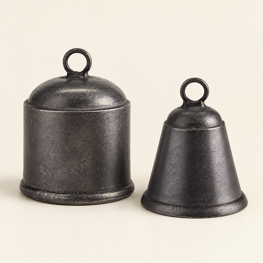 Two cast-aluminum bells in an antique-pewter finish, showing their cylindrical and tapered shapes on an ivory surface.