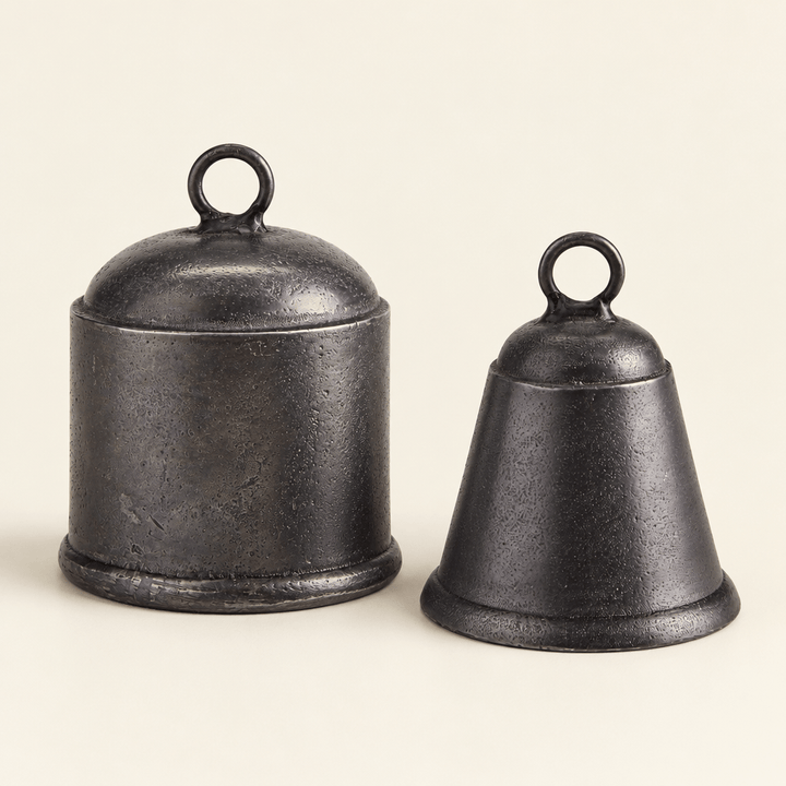 Two cast-aluminum bells in an antique-pewter finish, showing their cylindrical and tapered shapes on an ivory surface.