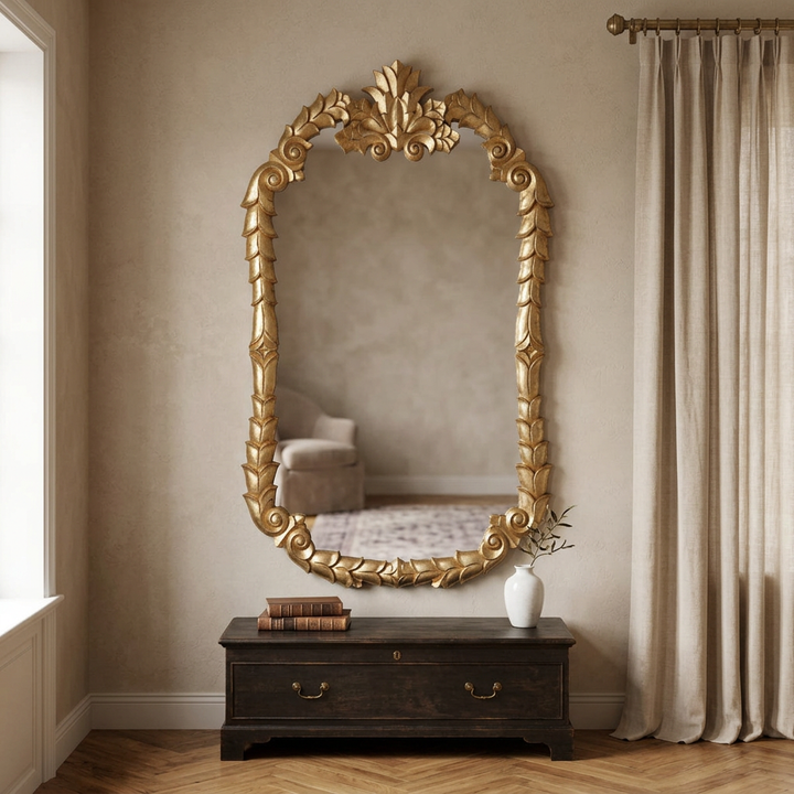 Soft Gold Colette carved wood wall mirror above a dark wood chest in a softly lit French-inspired living room.