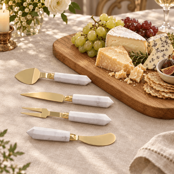 White marble and gold cheese utensils styled beside cheeses and grapes on a wooden serving board