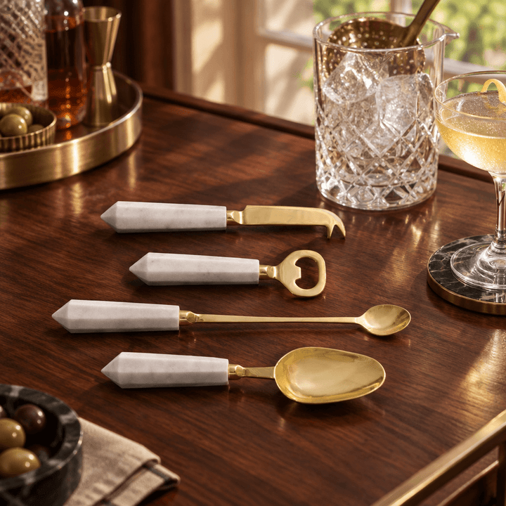 White marble and gold cocktail tool set styled on a walnut home bar with glassware.