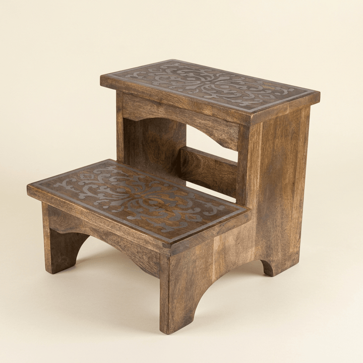 Belvedere two-step mango wood stool with ornate metal inlay on both treads and arched wooden supports against an ivory studio background.