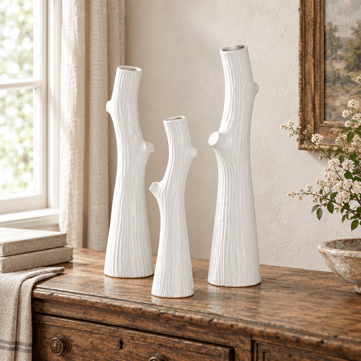 Three white ceramic branch-shaped vases in graduated heights on an antique wooden console.