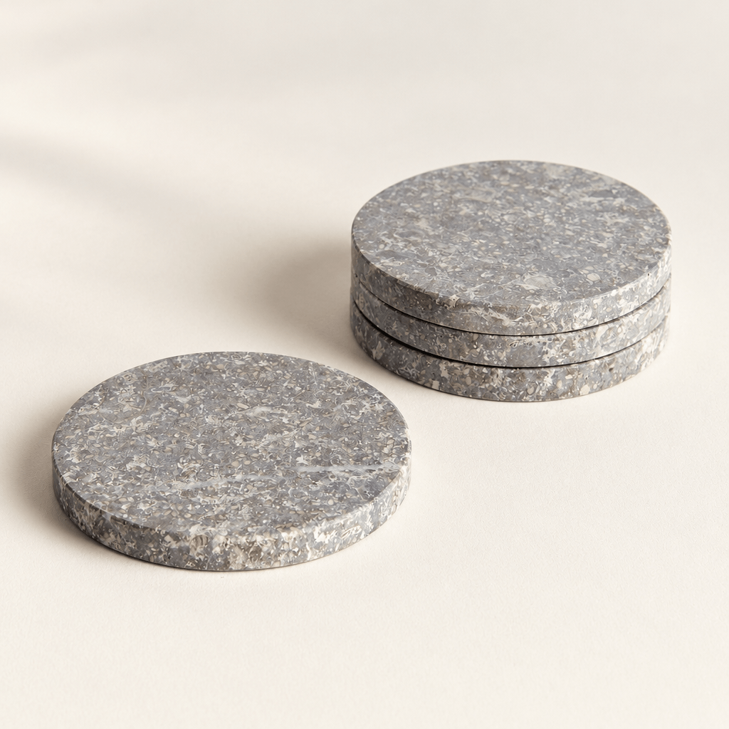 Three round gray marble coasters stacked beside a single coaster on an ivory surface.