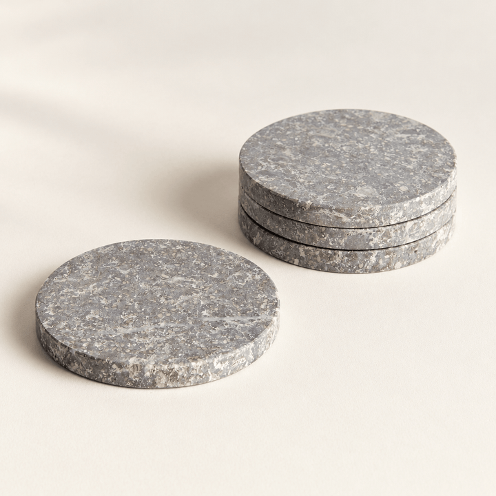 Three round gray marble coasters stacked beside a single coaster on an ivory surface.