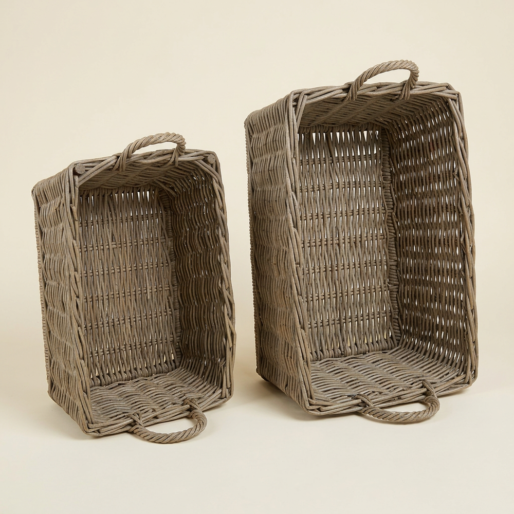Two gray woven rattan baskets with loop handles displayed upright on their sides against an ivory studio background.
