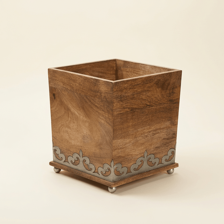 Belvedere square mango wood waste basket with silver-tone scrollwork inlay and small metallic feet on an ivory background.