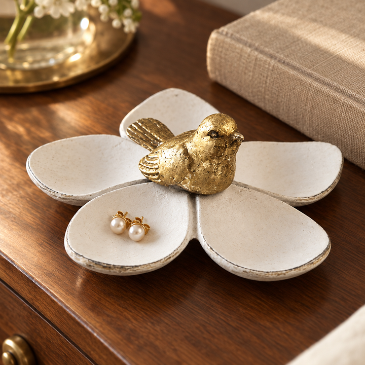 White flower jewelry dish with gold bird and stud earrings on a walnut bedside table