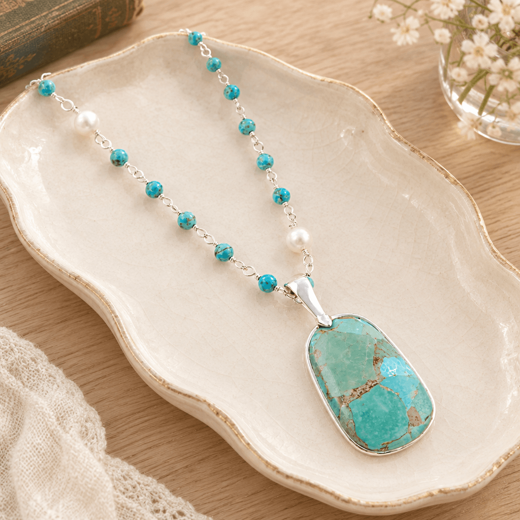 Turquoise and pearl sterling silver pendant necklace styled on a cream ceramic jewelry tray