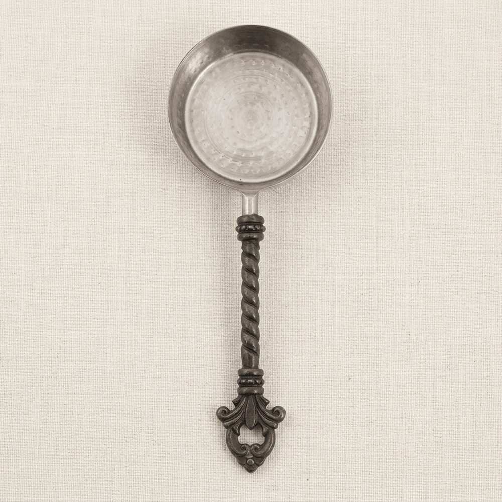 Overhead detail of one Bellavita measuring cup showing its stainless steel bowl, twisted dark handle and fleur-de-lis end