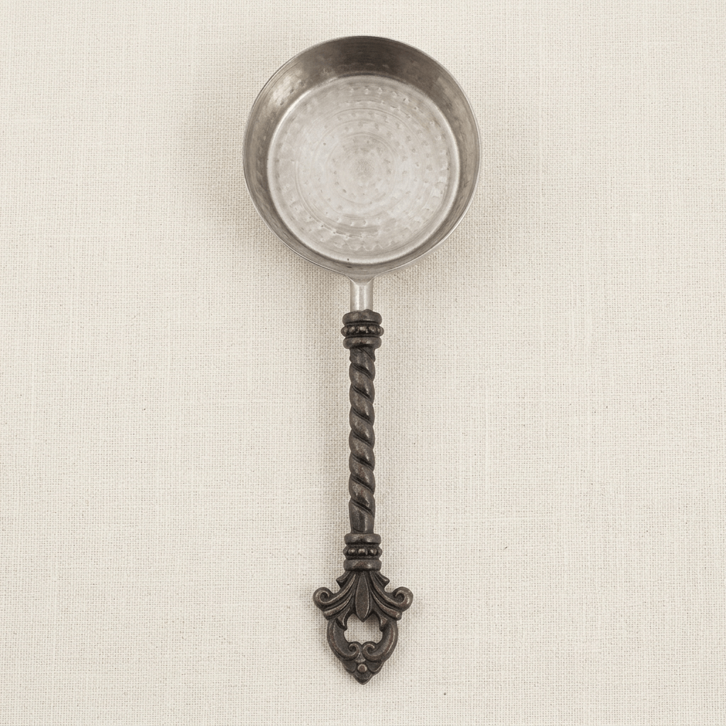 Overhead detail of one Bellavita measuring cup showing its stainless steel bowl, twisted dark handle and fleur-de-lis end