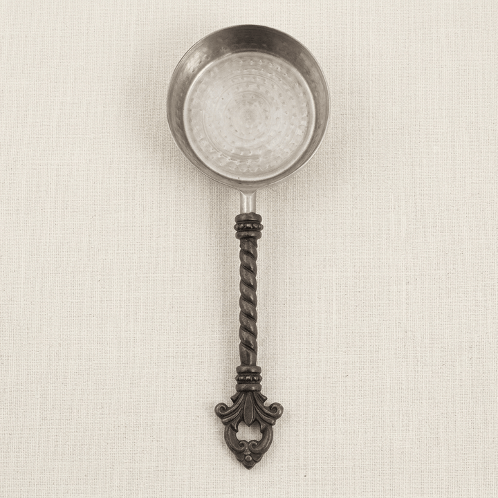 Overhead detail of one Bellavita measuring cup showing its stainless steel bowl, twisted dark handle and fleur-de-lis end