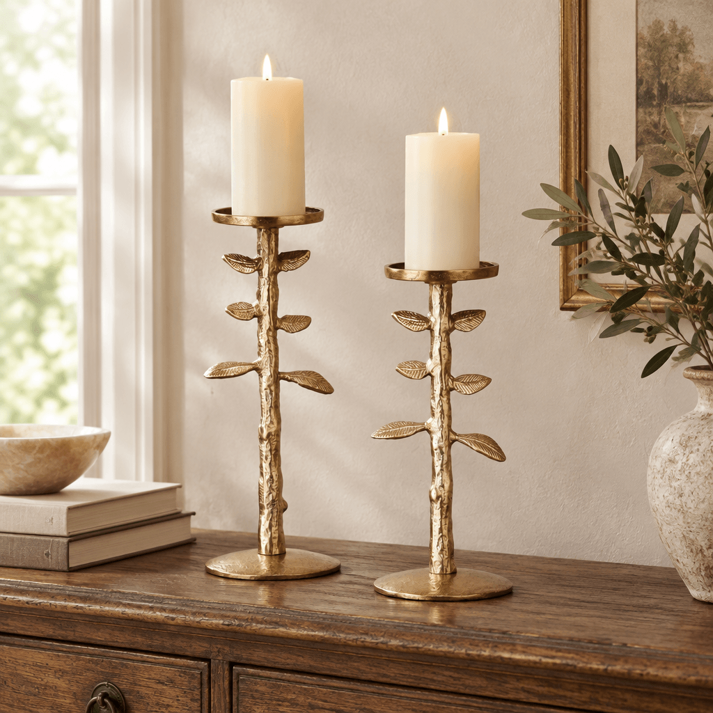 Gold botanical candle stands in graduated heights with ivory pillar candles on an antique wooden console.
