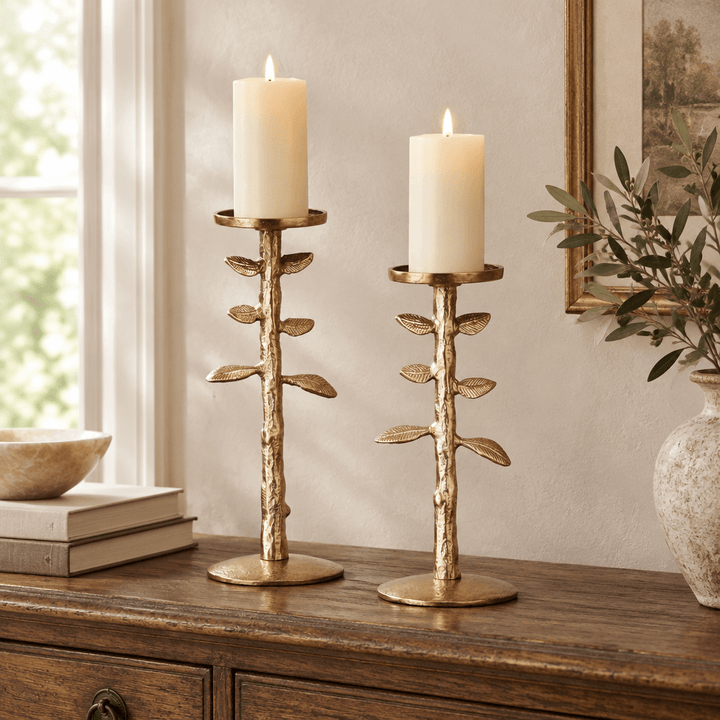 Gold botanical candle stands in graduated heights with ivory pillar candles on an antique wooden console.