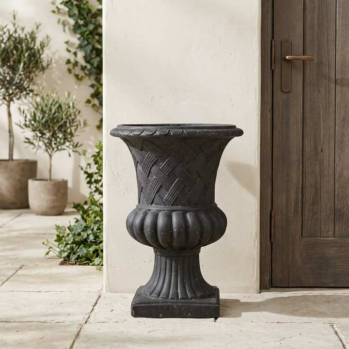 Black Trevi Lattice Weave Urn Planter with basketweave texture and a fluted pedestal beside a wooden entry door.