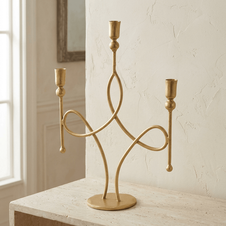 Three-arm antique gold iron scrollwork candelabra on a pale limestone console in natural light.
