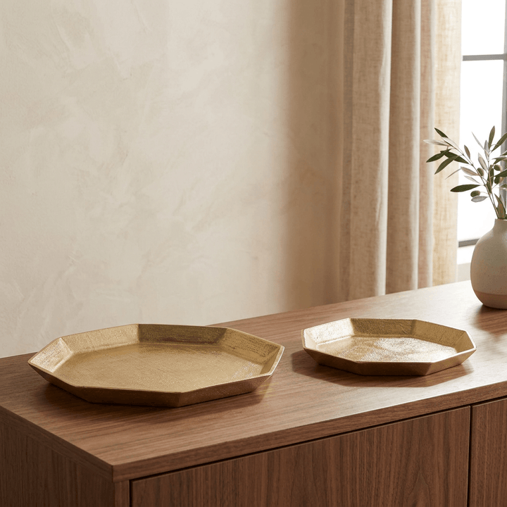 Pair of gold octagonal serving trays displayed on a walnut sideboard in a softly lit interior.