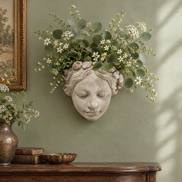 Cement Sun Goddess Wall Planter with botanical stems styled on a sage green wall above a wooden console.