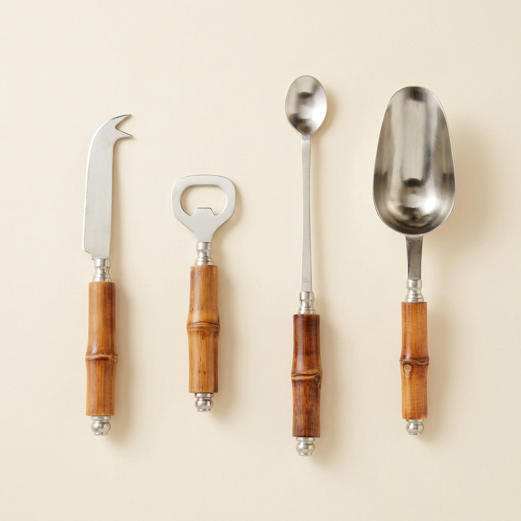 Four stainless steel cocktail tools with brown bamboo handles arranged on an ivory studio background.