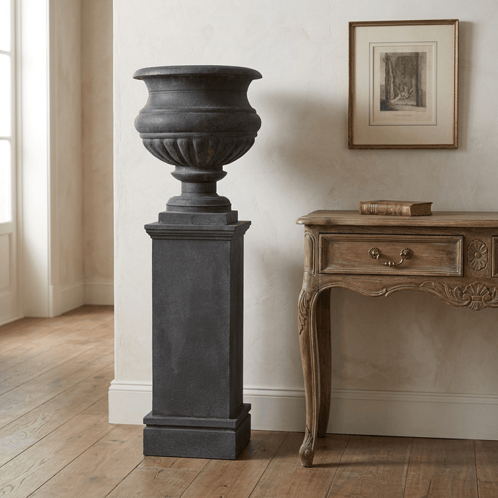 Montclair Iron Urn with Pedestal in Black, shown empty beside a wooden console in a traditional entry.