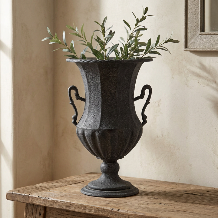 Valmont Scrolled Iron Amphora Urn in Black, styled with leafy branches on an aged wooden entry console.